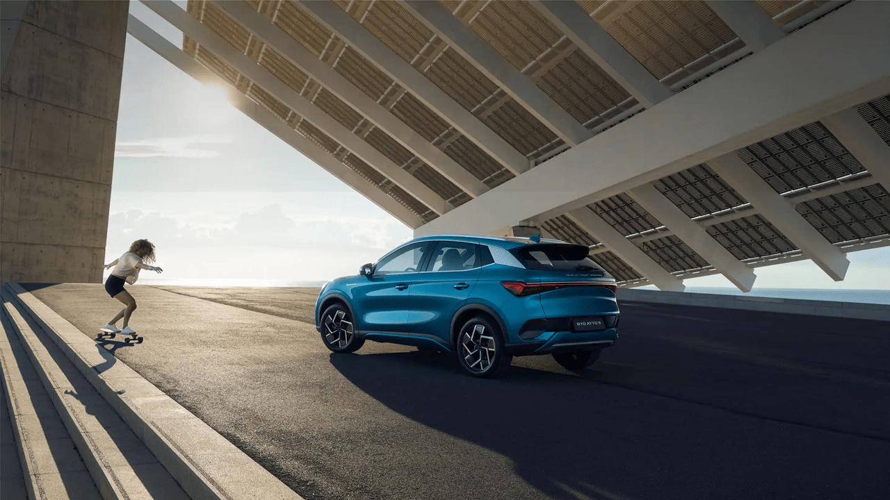 Femme sur un skate-board à côté d'une Atto 3 en finition bleue